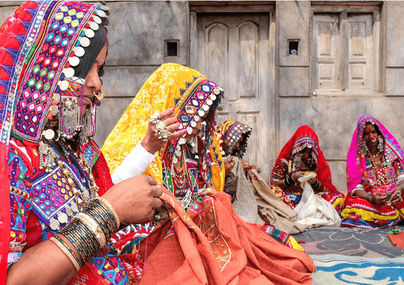 Banjara women sitting together outdoors, hand-embroidering mirror-work textiles