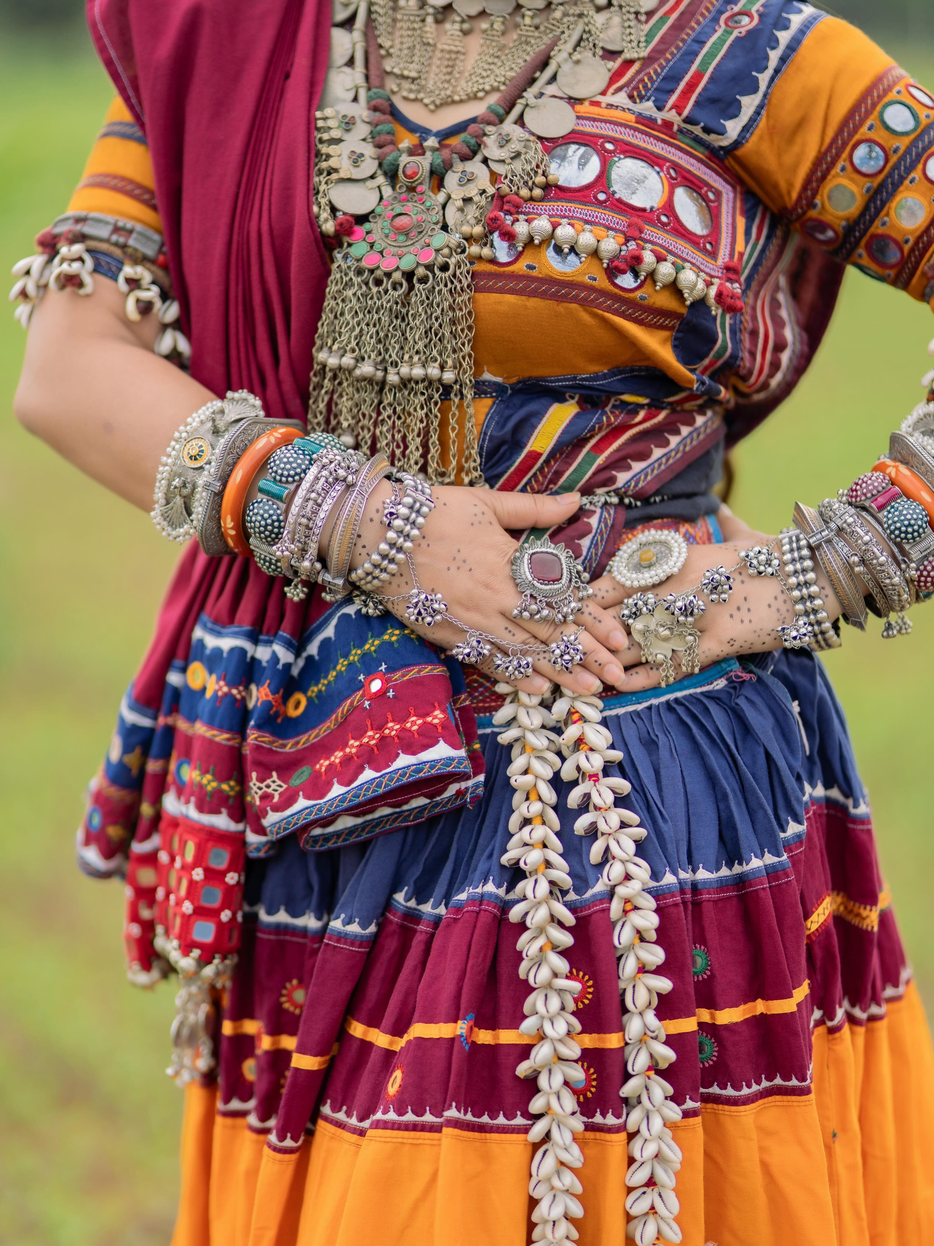 Hands with silver rings and bangles resting on a mirror-work skirt with cowrie-shell strings