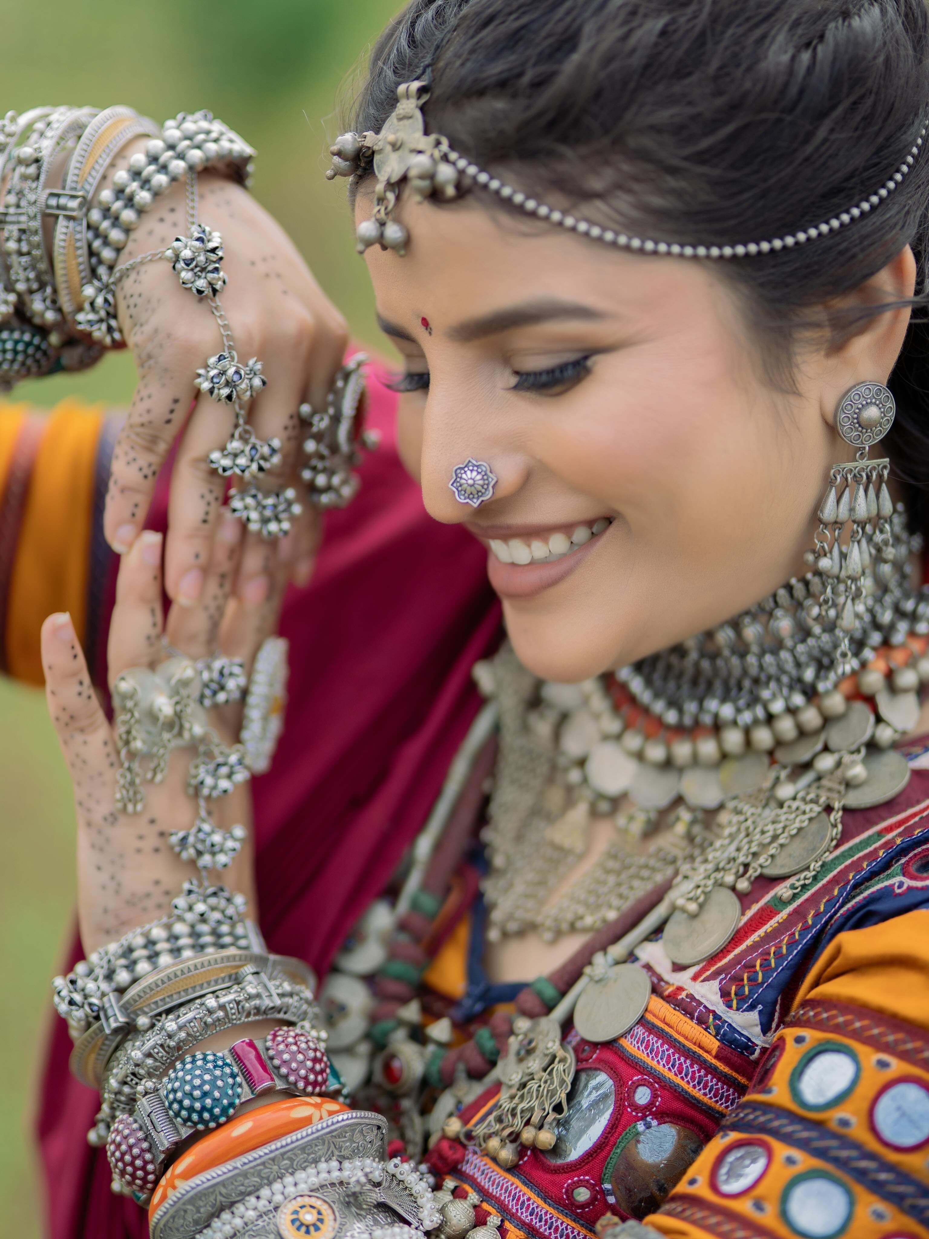 A smiling Banjara woman wearing a silver head ornament, nose ring and stacked bangles