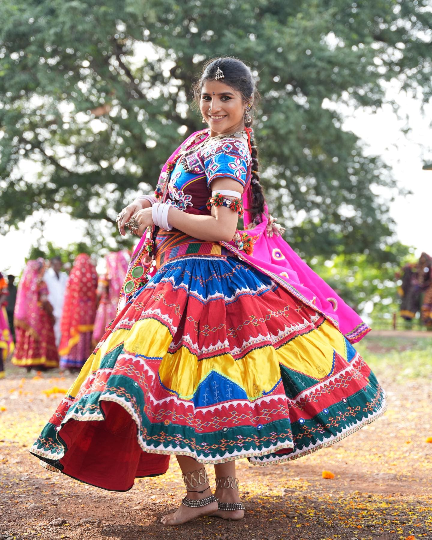 A Banjara woman dancing in a green field in a mirror-work skirt, maroon dupatta and silver jewellery